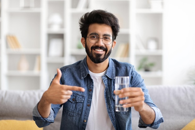 Glimlachende Indiase man die een glas water vasthoudt en ernaar wijst