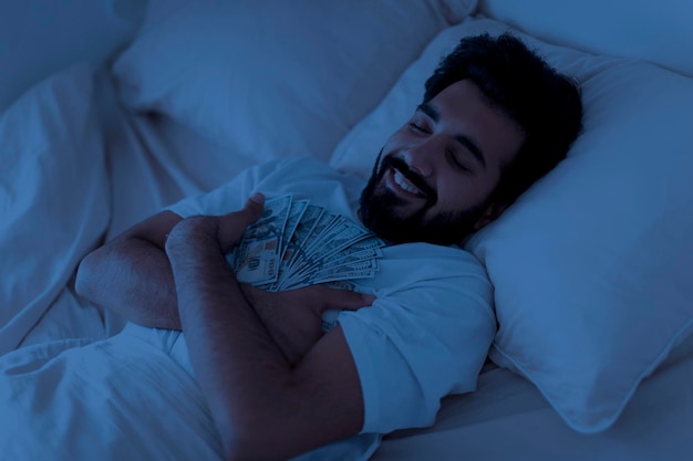 Glimlachende Indiase man die in de nacht met dollar contant in de hand spiedt.