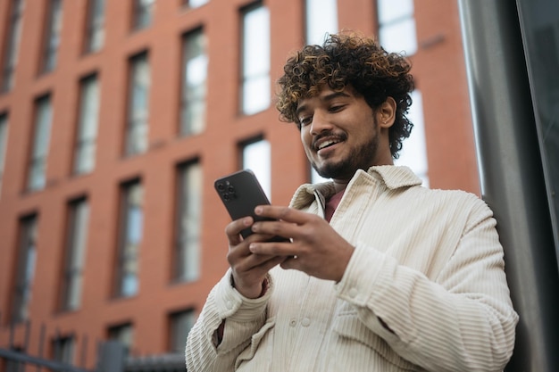 Foto glimlachende indiase man met mobiele telefoon die tekstbericht leest, communicatie online buiten