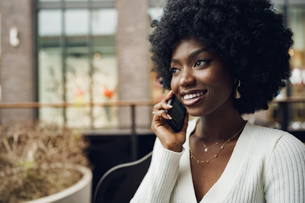 Glimlachende jonge Afrikaanse vrouw die op cellphone bij koffie spreekt