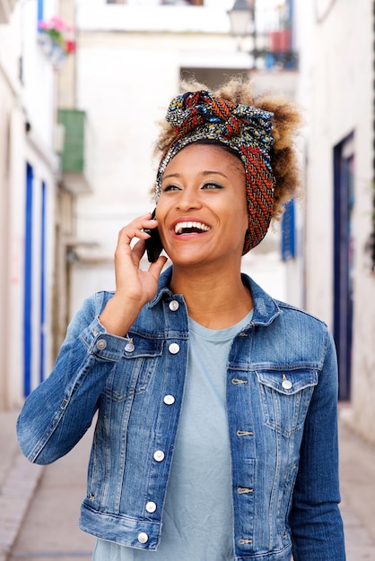 Glimlachende jonge Afrikaanse vrouw die telefoongesprek in openlucht maakt