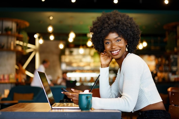 Glimlachende jonge Afrikaanse vrouw zitten met laptop in café