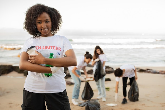Glimlachende jonge afro-amerikaanse dame houdt flessen vast en multiraciale mensen vrijwilligers in t-shirts met