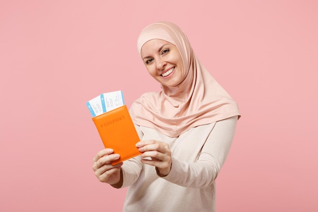 Glimlachende jonge Arabische moslimvrouw in hijab lichte kleding poseren geïsoleerd op roze achtergrond. Mensen religieuze islam levensstijl concept. Bespotten kopie ruimte. Houden van paspoort, instapkaart ticket.