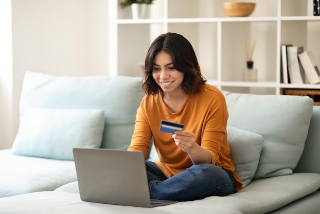 Glimlachende jonge Arabische vrouw die online winkelen met laptop en creditcard maakt