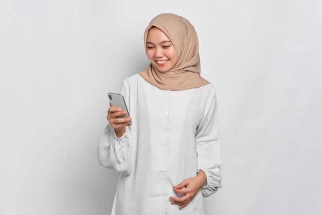 Glimlachende jonge Aziatische moslimvrouw die een mobiele telefoon gebruikt, ontving goed nieuws geïsoleerd op een witte achtergrond