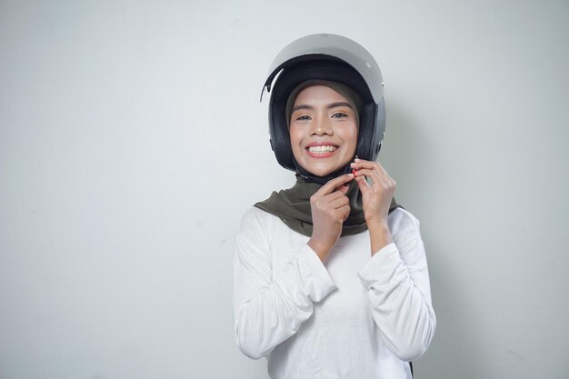Glimlachende jonge Aziatische moslimvrouw die motorhelm gebruiken die op witte achtergrond wordt geïsoleerd