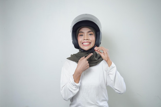 Glimlachende jonge Aziatische moslimvrouw die motorhelm gebruiken die op witte achtergrond wordt geïsoleerd