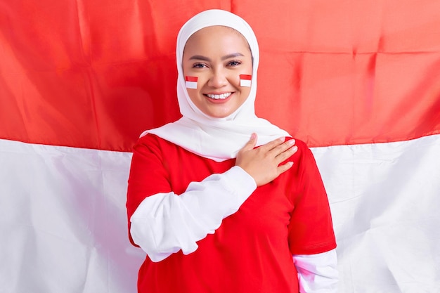 Glimlachende jonge Aziatische moslimvrouw in rood witte tshirt groet aan het vieren van de onafhankelijkheidsdag van Indonesië op 17 augustus geïsoleerd op vlag Indonesische achtergrond