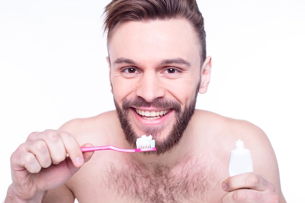 Glimlachende jonge bebaarde man met tandenborstel die tanden schoonmaakt en naar de badkamer kijkt Gezondheidszorg mondhygiëne mensen en schoonheidsconcept