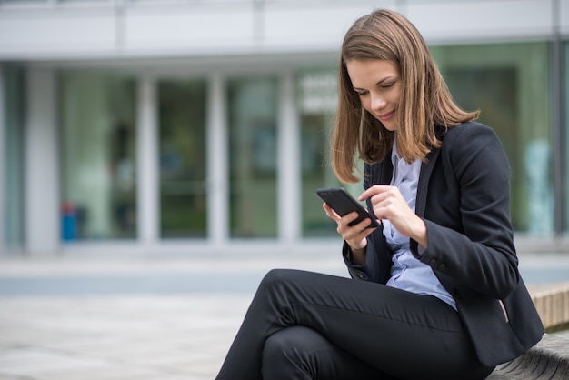 Glimlachende jonge bedrijfsvrouw die haar mobiele celtelefoon met behulp van