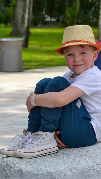 Foto glimlachende jonge blonde jongen zit op een bankje in het tuinpark op een zonnige dag