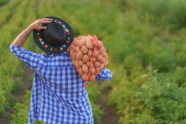 Glimlachende jonge boer die een zak verse aardappelen vasthoudt op een groen aardappelveld