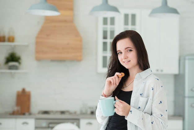 Glimlachende jonge brunette vrouw in de keuken met een kopje thee en bagels