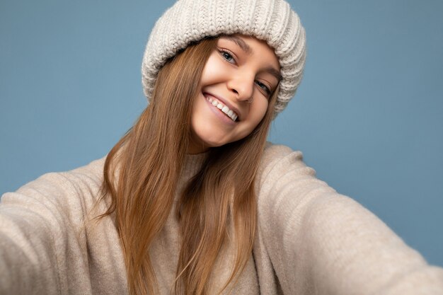 Glimlachende jonge donkere blonde vrouw die zich geïsoleerd over kleurrijke muur als achtergrond bevindt die alledaagse trendy kleding draagt die camera bekijkt die gezichtsemoties toont.