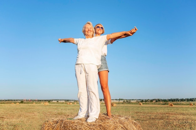 Glimlachende jonge en oude vrouwen staan op een hooiberg in een veld bij zonsondergang Rust en ontspanning