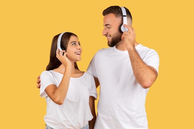 Glimlachende jonge Europese man in wit T-shirt en dame in draadloze koptelefoon luisteren naar muziek.