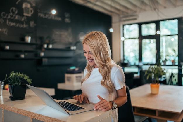 Glimlachende jonge freelancer die laptop in modern coworking bureau met behulp van.