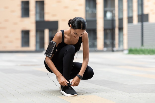 Glimlachende jonge islamitische dame in sportkleding met telefoon op schouder fitness tracker veters strikken