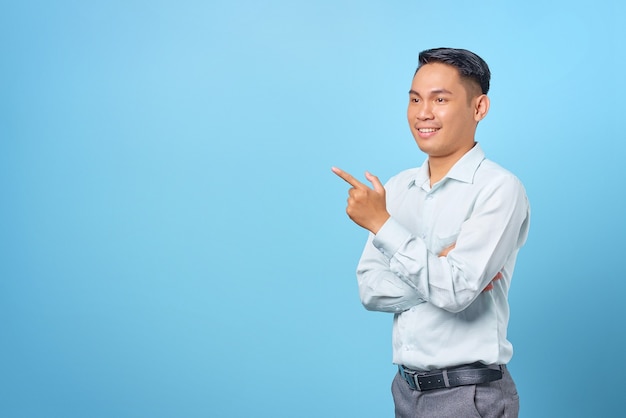 Glimlachende jonge knappe zakenman wijzende vinger weg naar kopieerruimte op blauwe achtergrond