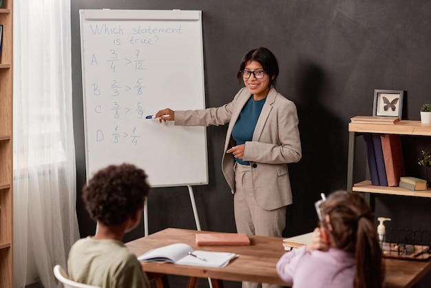 Glimlachende jonge latijns-leraar wijzend naar een voorbeeld op het whiteboard terwijl hij een nieuw onderwerp aan school uitlegt c