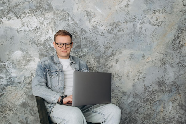 Glimlachende jonge man aan het werk op grijze achtergrond die e-mail controleert in de ochtend die een bericht schrijft