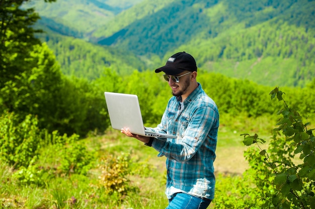 Glimlachende jonge man aan het werk op laptop in de frisse lucht in de bergen