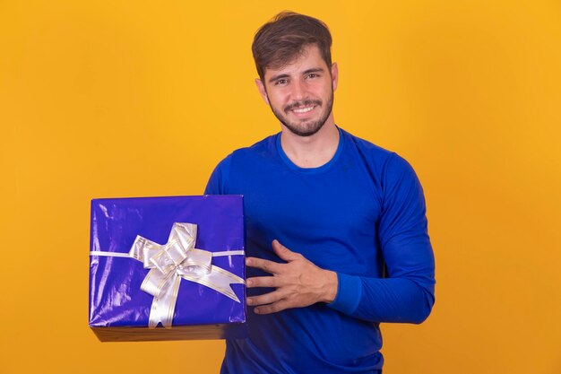 Glimlachende jonge man die een geschenkdoos op gele achtergrond houdt Jonge jongen die een geschenkdoos op gele achtergrond houdt