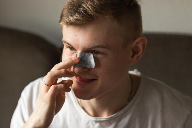 Foto glimlachende jonge man die een zwarte neusplakker aanbrengt om de huid van de poriën te reinigen en acne of zwarte punten op de neus te verwijderen