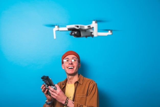 Foto glimlachende jonge man leert een drone te besturen met een afstandsbediening op een blauwe achtergrond