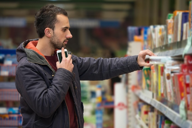 Glimlachende jonge man met behulp van mobiele telefoon tijdens het winkelen in de winkel