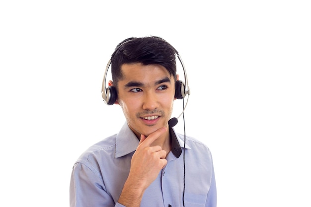 Glimlachende jonge man met donker haar in blauw shirt met zwarte koptelefoon op witte achtergrond in studio