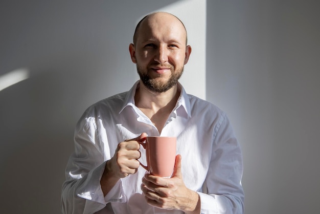 Glimlachende jonge man met een baard die koffie drinkt in de zon