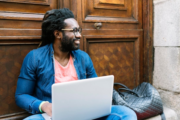 Glimlachende jonge man met een laptop terwijl hij in de stad zit