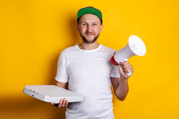 Glimlachende jonge man met een megafoon met verpakte pizza op een gele achtergrond