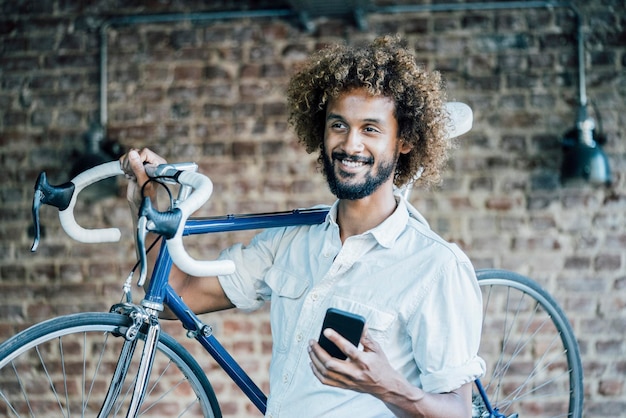 Glimlachende jonge man met fiets en mobiele telefoon