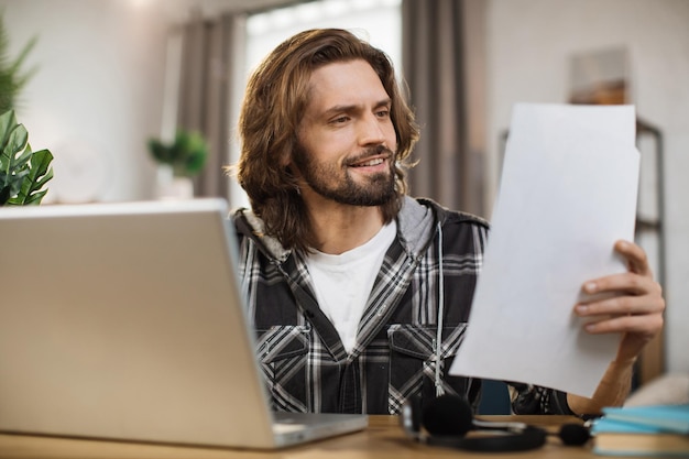 Glimlachende jonge man met videoconferentie op laptop terwijl hij thuis werkt
