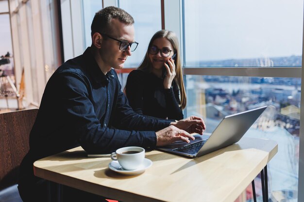 Glimlachende jonge mannelijke en vrouwelijke manager die aan tafel zit te kijken naar een computerscherm en bedrijfssoftware uit te leggen of samen met collega's aan een online project te werken