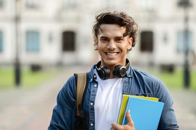 Glimlachende jonge mannelijke student met werkboeken en rugzak die buiten staat