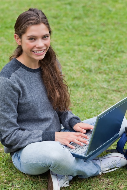 Glimlachende jonge meisjeszitting neer in een park terwijl het gebruiken van haar laptop