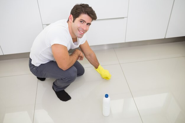 Glimlachende jonge mens die de keukenvloer schoonmaakt