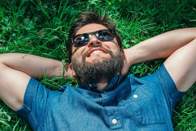 Glimlachende jonge mens die en op groen gras ligt ontspant