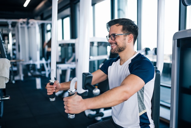 Glimlachende jonge mens die in de gymnastiek uitwerkt.