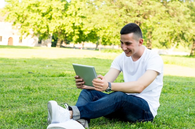 Foto glimlachende jonge mens met tablet in park