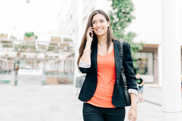 Glimlachende jonge mensen praten op hun mobiele telefoon terwijl ze op het voetpad in de stad lopen.