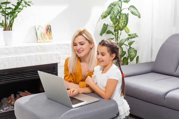 glimlachende jonge moeder en dochter die online lessen studeren in een thuiskantoor in de moderne woonkamer