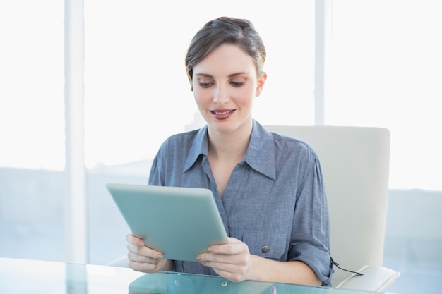 Glimlachende jonge onderneemsterzitting bij haar bureau die een tablet houden