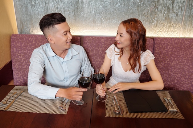 Glimlachende jonge vriend en vriendin kijken elkaar aan als ze met glazen wijn hun eerste verjaardag vieren