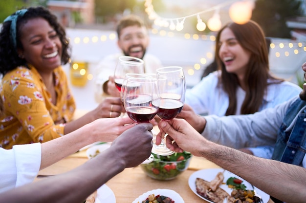 Foto glimlachende jonge vrienden drinken rode wijn op het dak barbecue mensen drinken en eten buiten