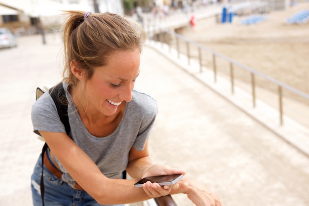 Glimlachende jonge vrouw die celtelefoon bekijkt